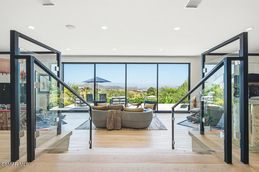Furnished living room with a curved sofa and floor-to-ceiling windows overlooking a patio and distant hills.
