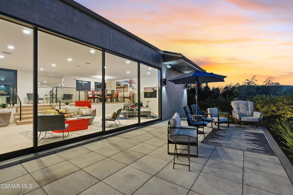 Modern home with a furnished patio and floor-to-ceiling glass doors at sunset.