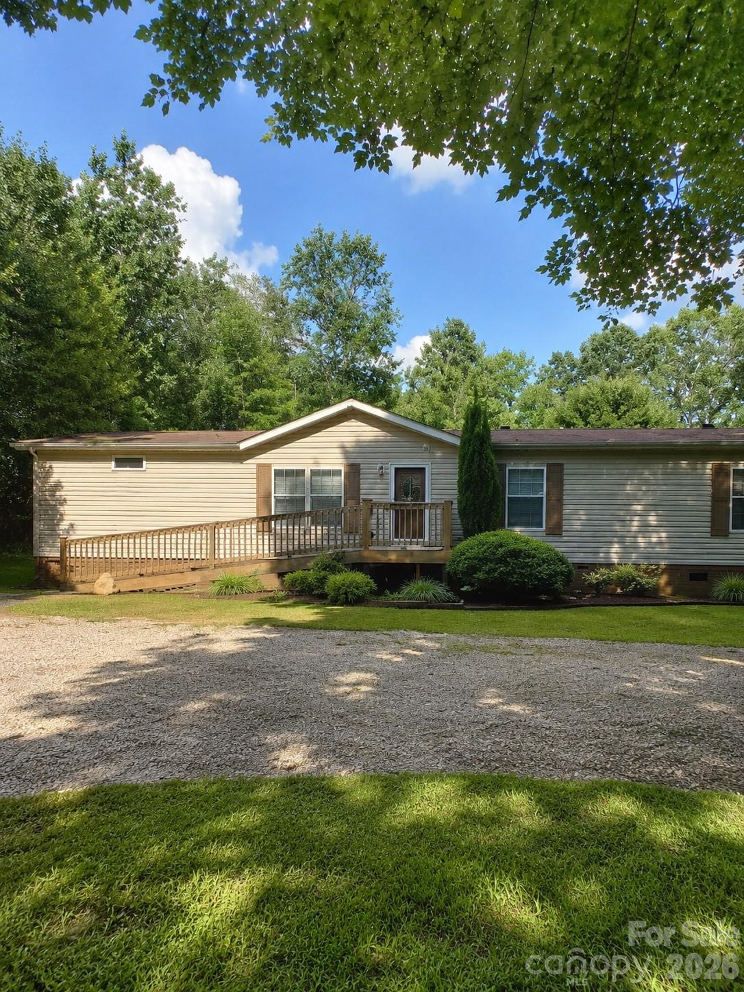 Beige single-story home with a raised wooden deck and ramp, surrounded by trees and lawn.