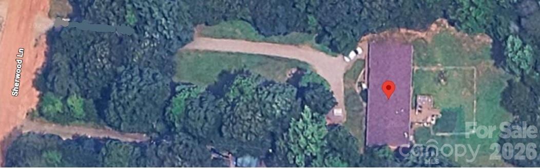 Aerial view of a house and curved driveway on a wooded lot, marked by a red location pin.