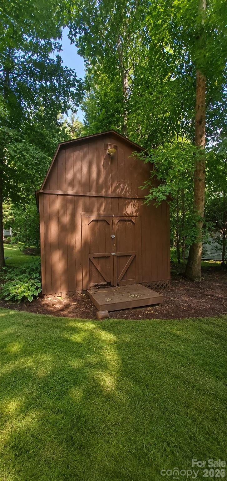 Brown wooden garden shed with double doors and a ramp, set among trees on a green lawn.