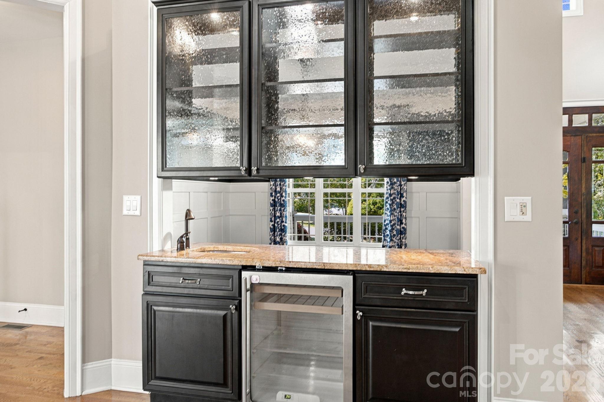 Kitchen beverage station with dark cabinets, granite counter, sink, and stainless steel beverage refrigerator.