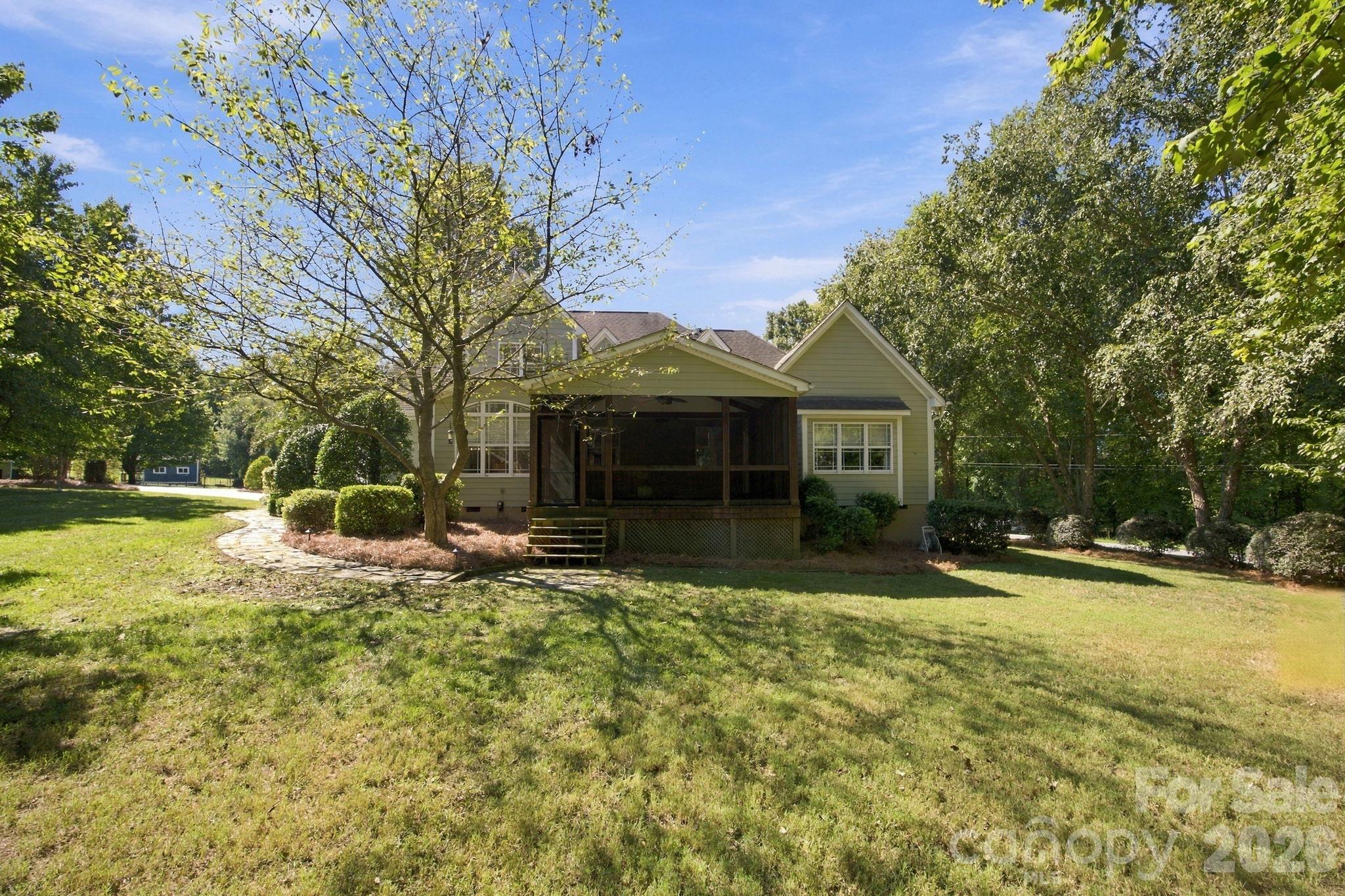House with a screened rear porch and stone path across a broad, tree-lined lawn.