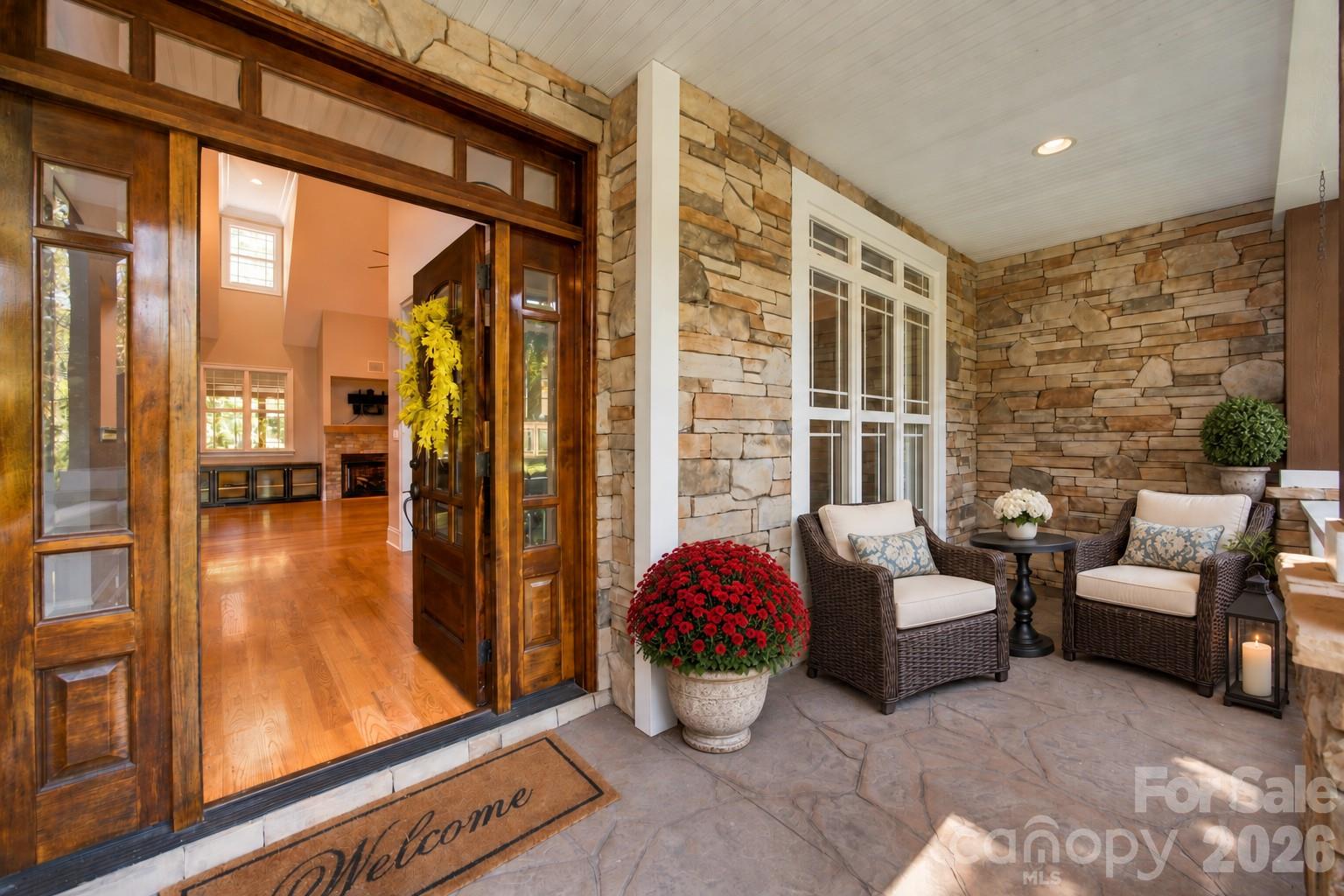 Covered stone porch with wicker chairs and an open wood-and-glass front door.