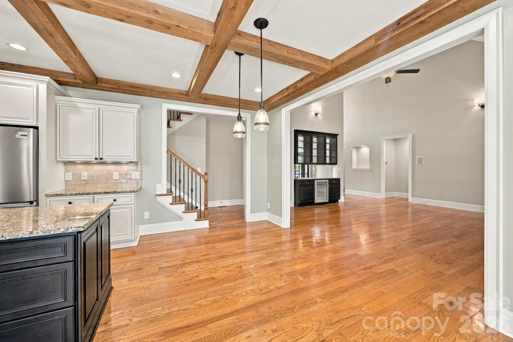 Open kitchen and living area with exposed wood ceiling beams, hardwood floors, and a black beverage bar.