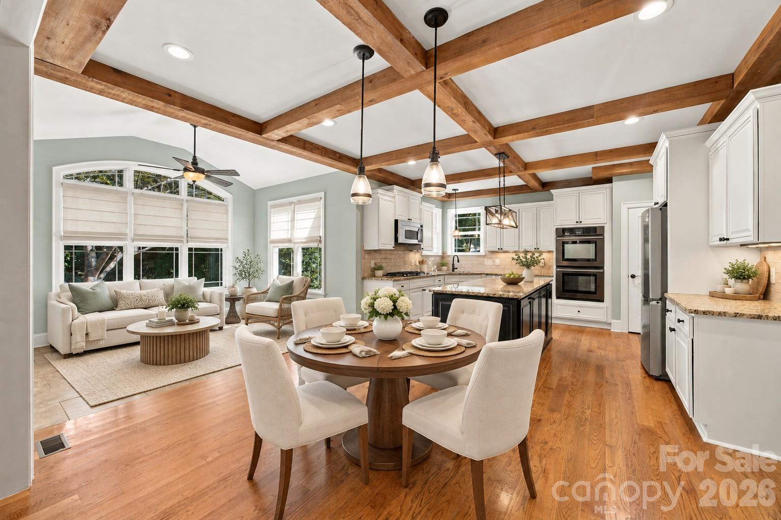 Open-plan kitchen, dining, and living area with exposed timber beams and white cabinetry.
