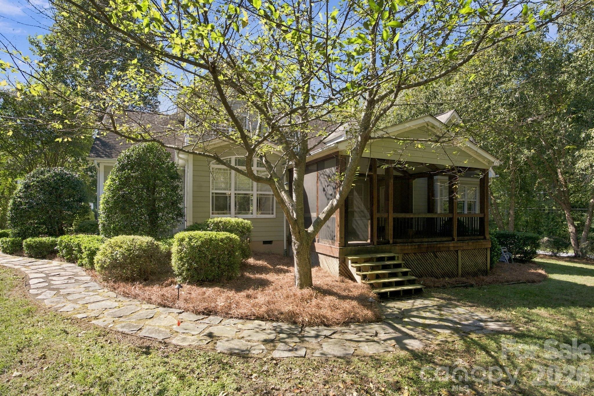 House with a covered screened porch, stone walkway, and mature trees.