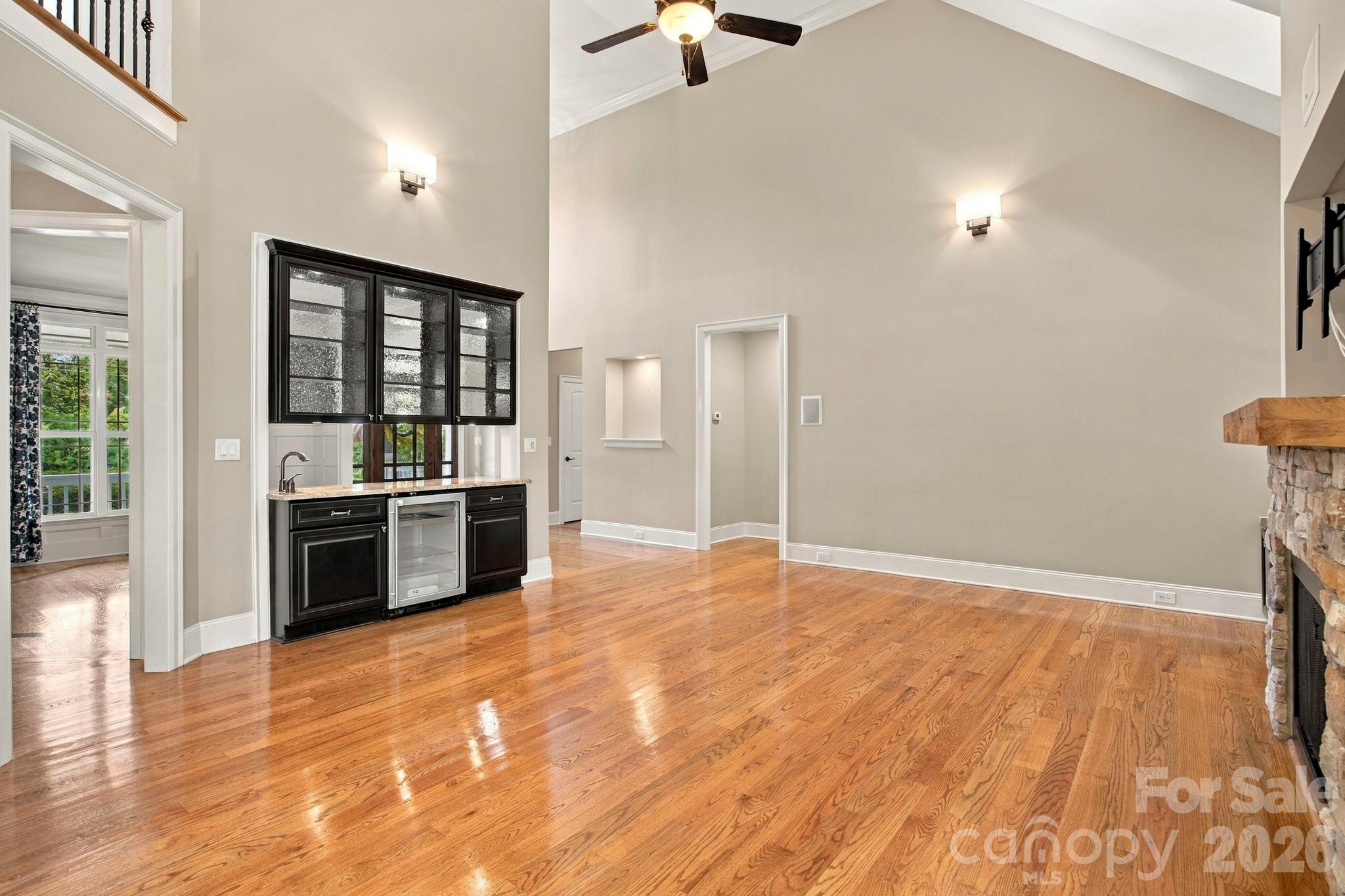 Vaulted living room with hardwood floors, stone fireplace, and black wet bar beneath leaded-glass windows.