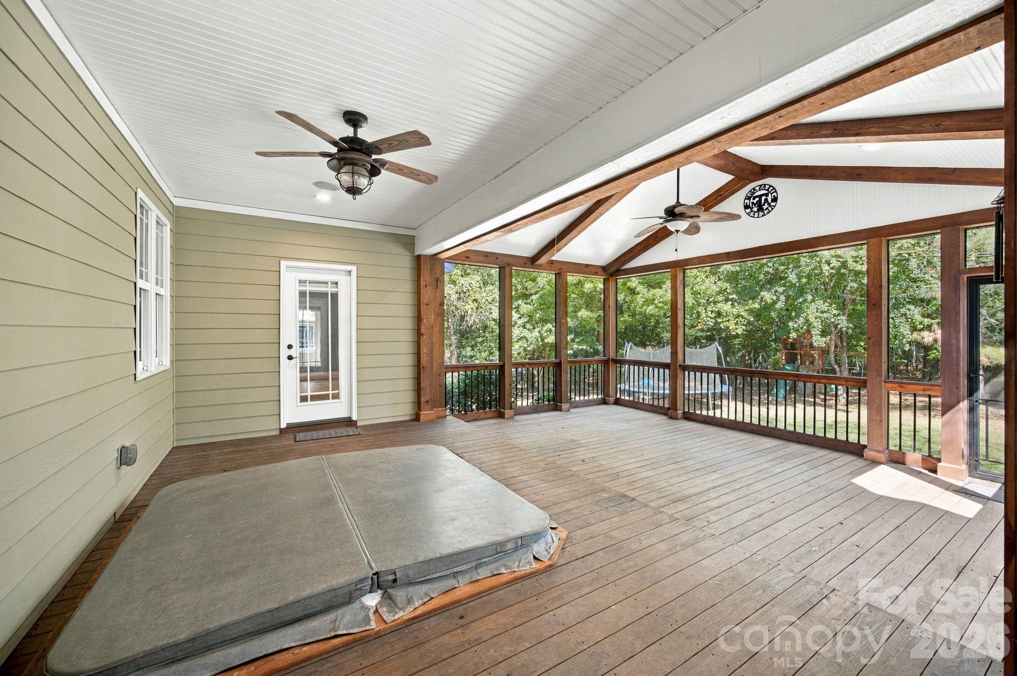 Screened porch with exposed timber beams, two ceiling fans, and a wooded yard beyond the railing.