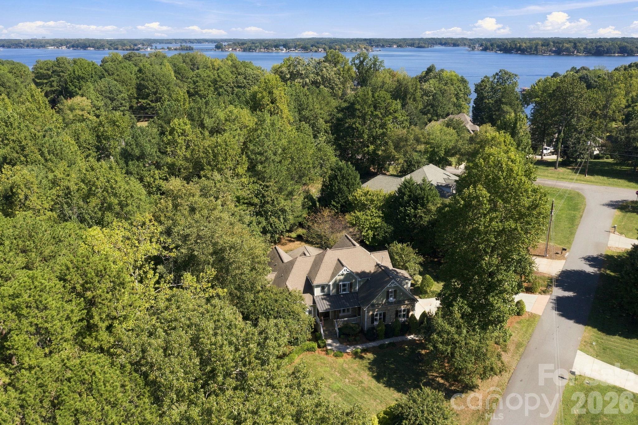 Aerial view of a tree-surrounded home with a lake beyond the neighborhood.
