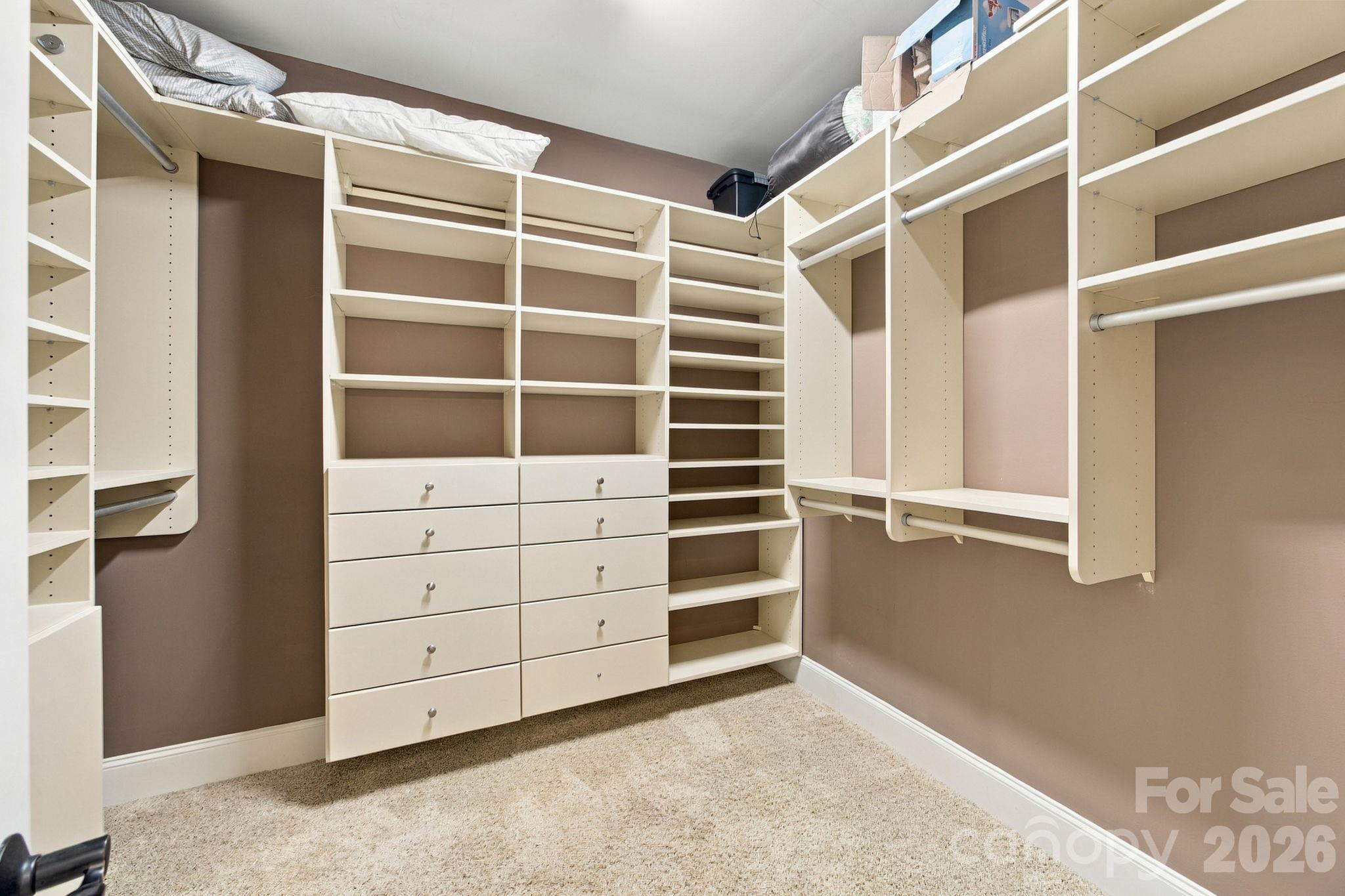 Walk-in closet with cream built-in shelves, hanging rods, and central drawers.