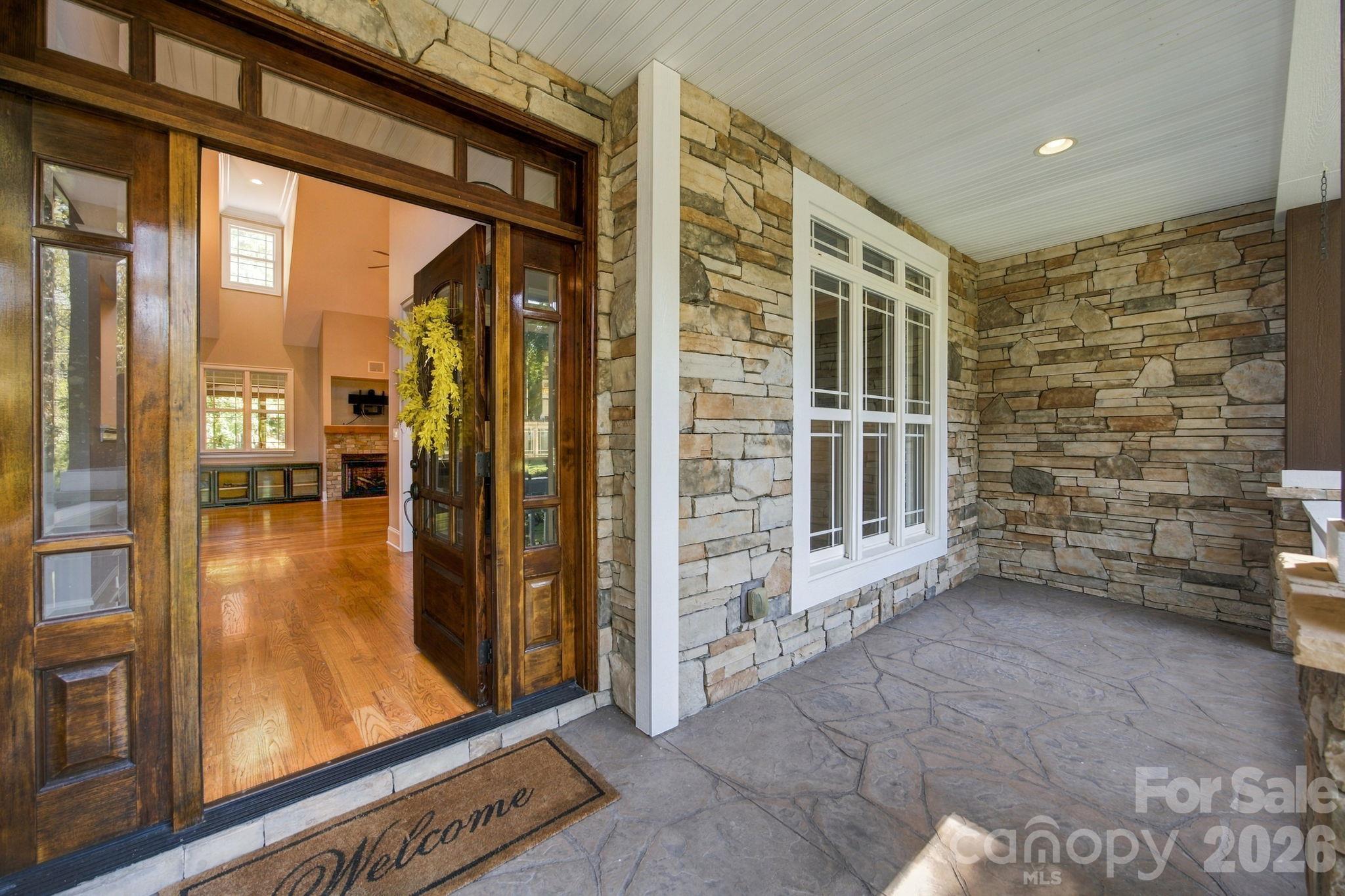 Stone-covered front porch with a dark wood entry door and a view of the living room fireplace.