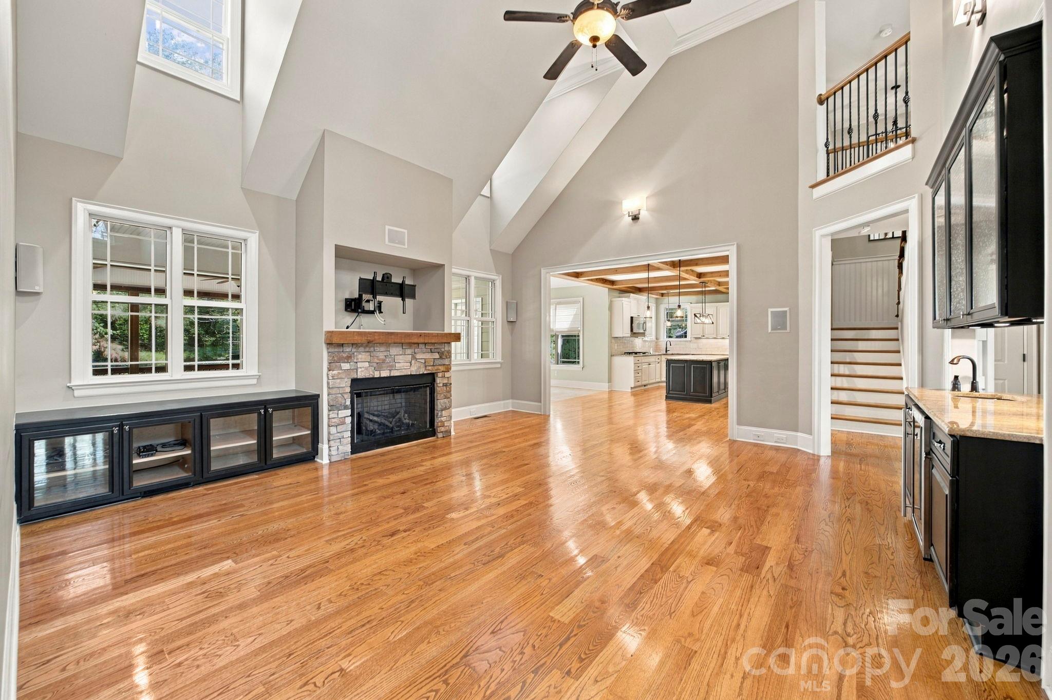 Vaulted living room with hardwood floors, stone fireplace, and an open view into the kitchen.