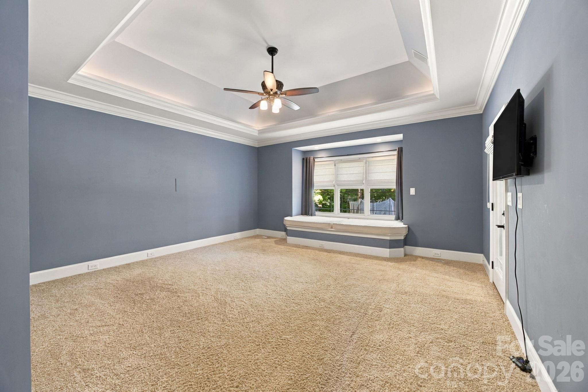 Mostly empty bedroom with a tray ceiling, carpet, and built-in window seat.