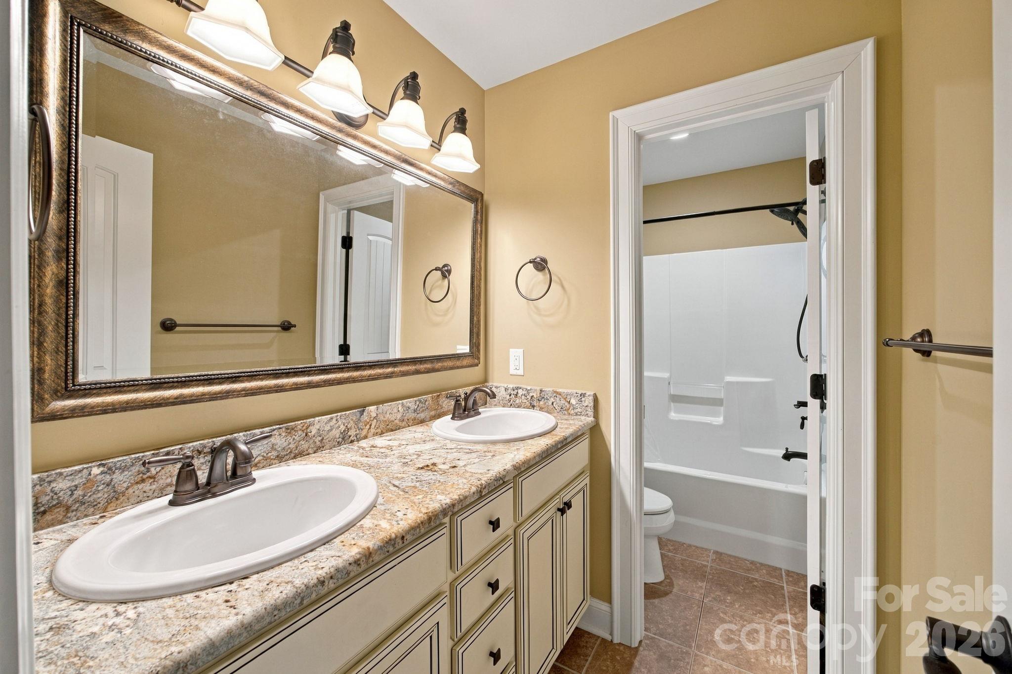 Bathroom with a double-sink stone vanity and an adjoining tub and shower.