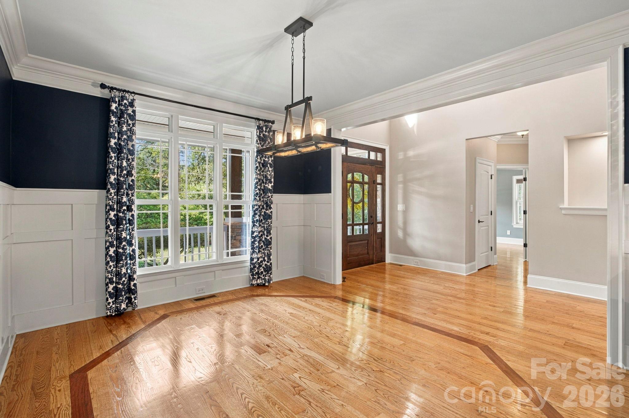 Vacant entry hall with a wood front door, large curtained windows, and hardwood floors with dark inlay.