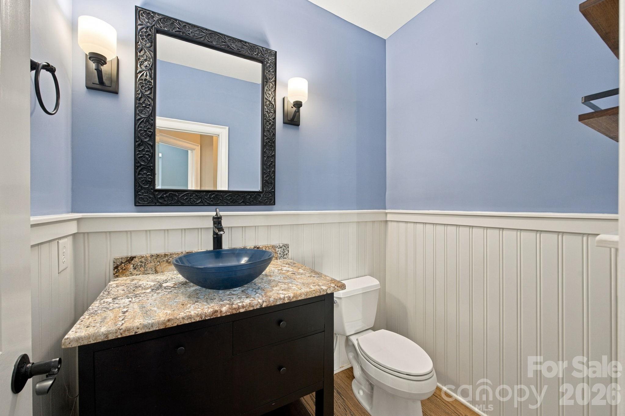 Bathroom with blue vessel sink, stone countertop, ornate mirror, and white beadboard wainscoting.