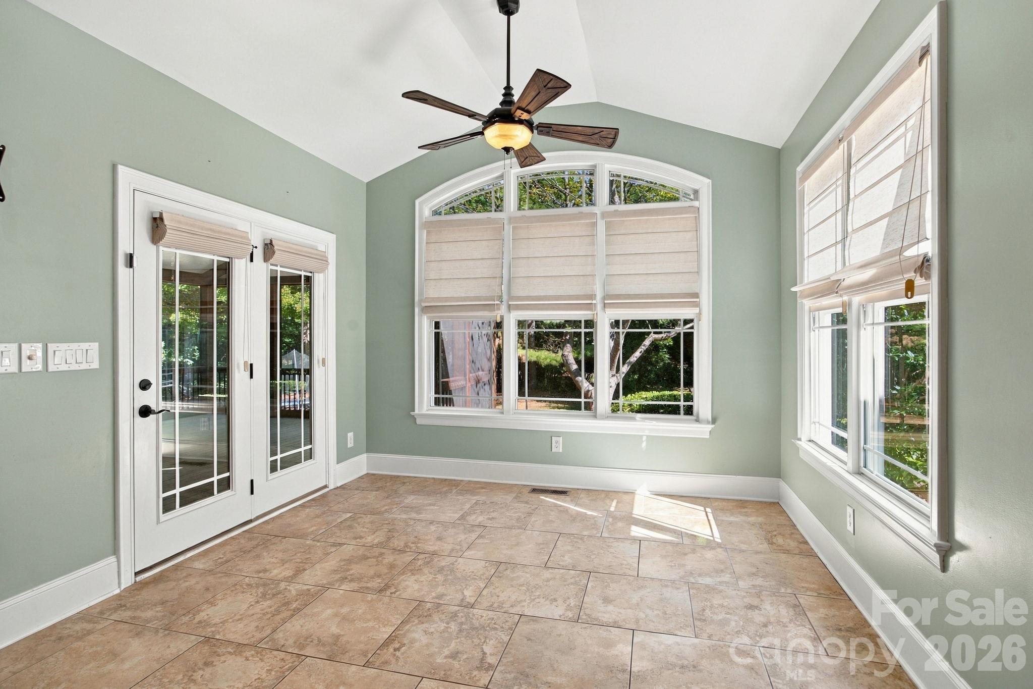 Unfurnished sunroom with vaulted ceiling, tan tile floor, French doors, and large shaded windows.