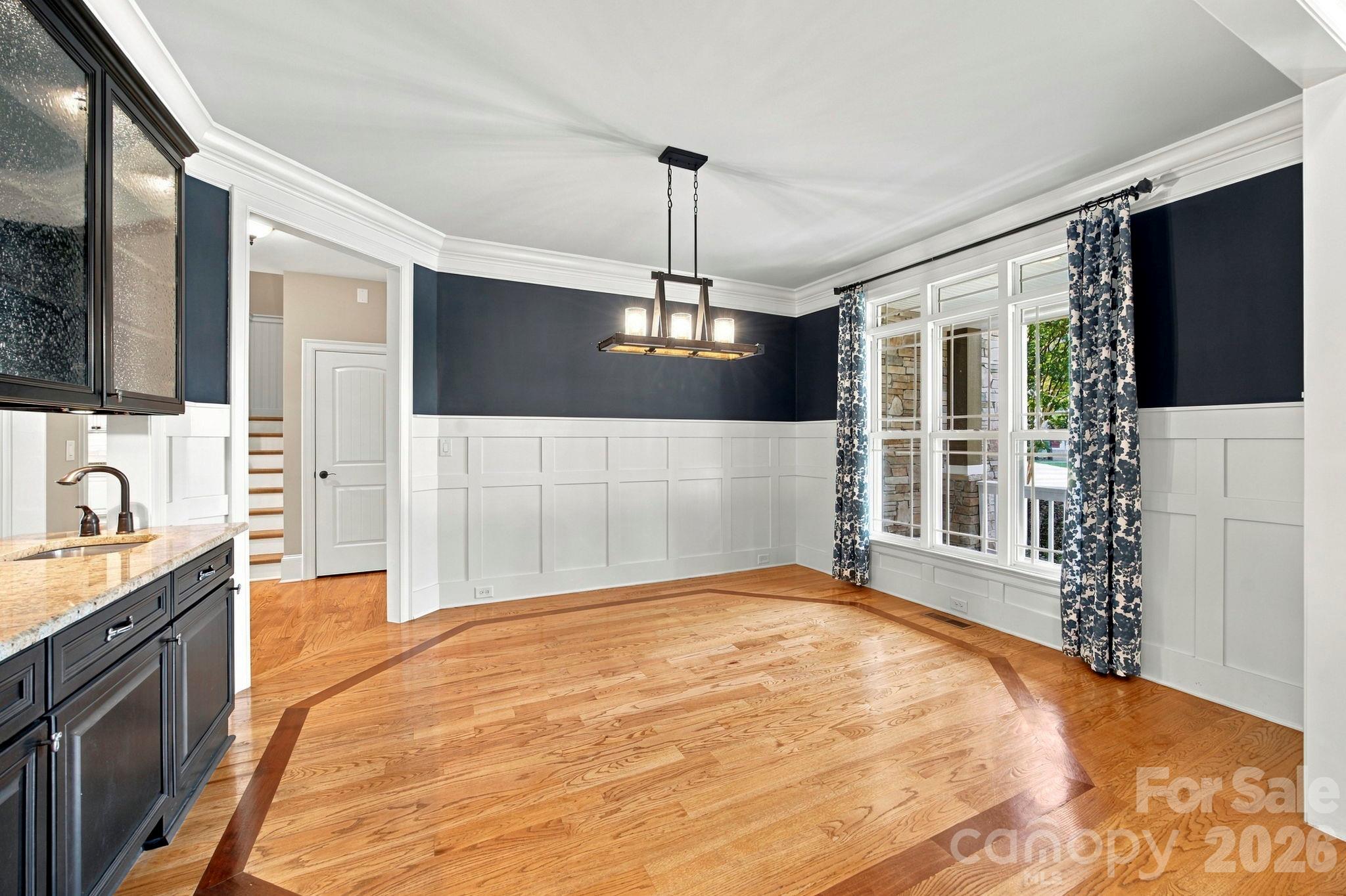 Unfurnished dining room with navy walls, white paneling, patterned curtains, and hardwood floors.