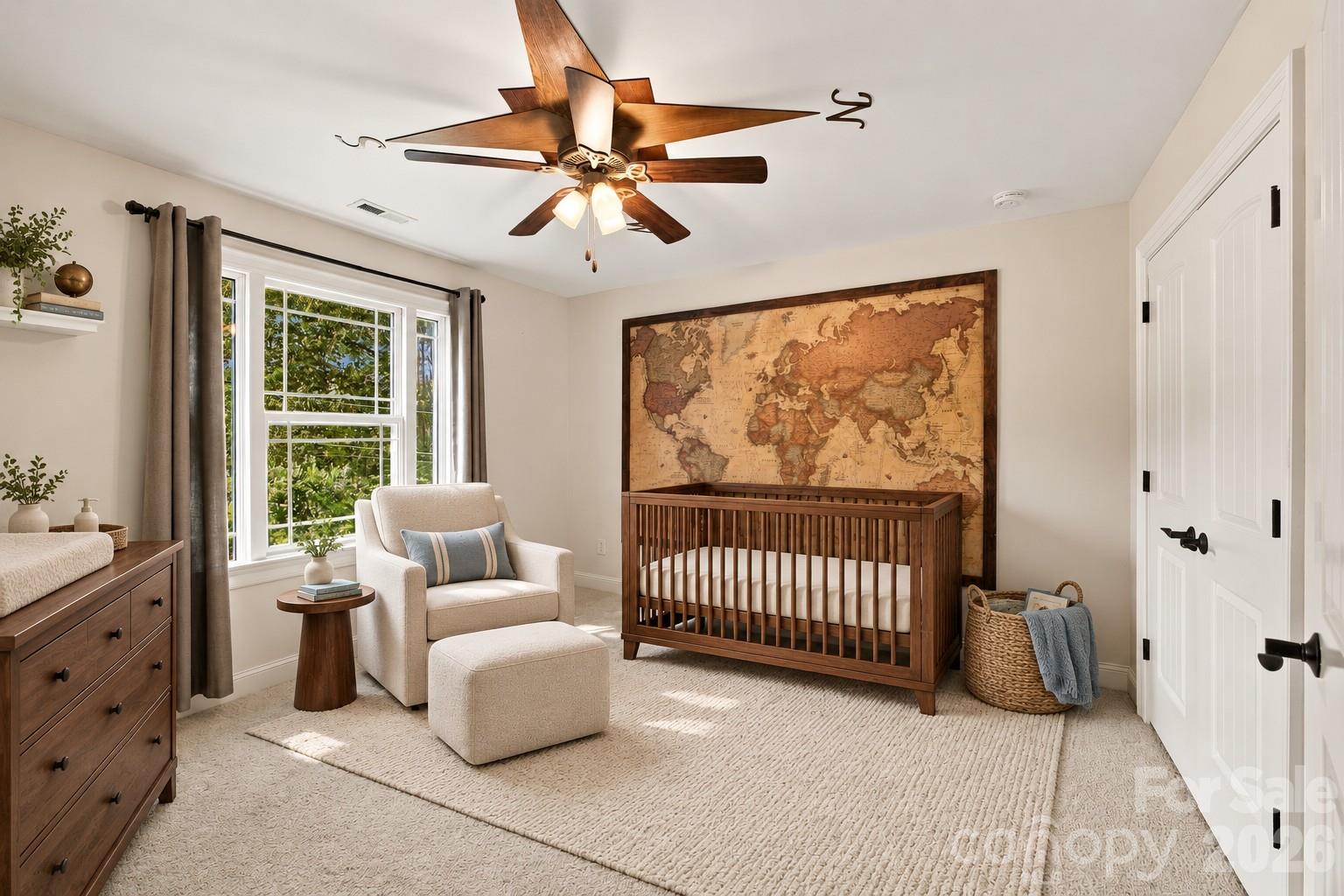 Staged nursery with a dark wood crib, large world map, cream armchair, and bright window.