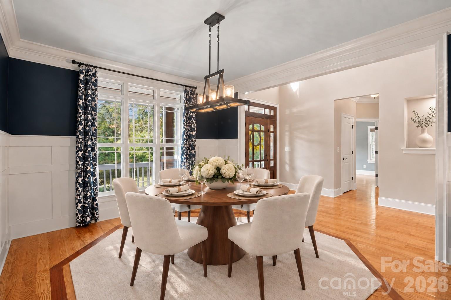 Dining room with a round wood table, navy accent walls, and large curtained windows.