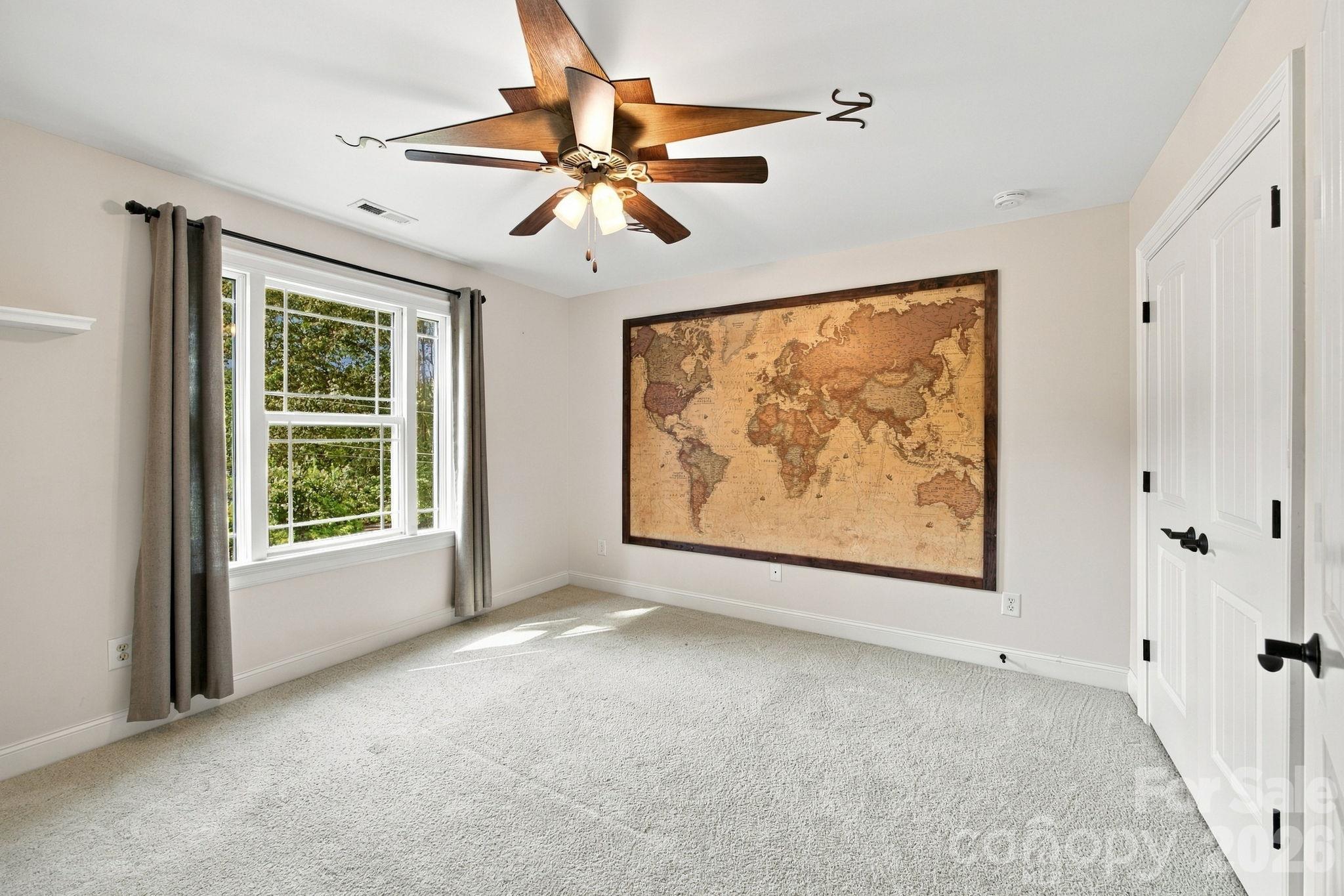 Unfurnished carpeted room with a large curtained window, wood ceiling fan, and framed world map.