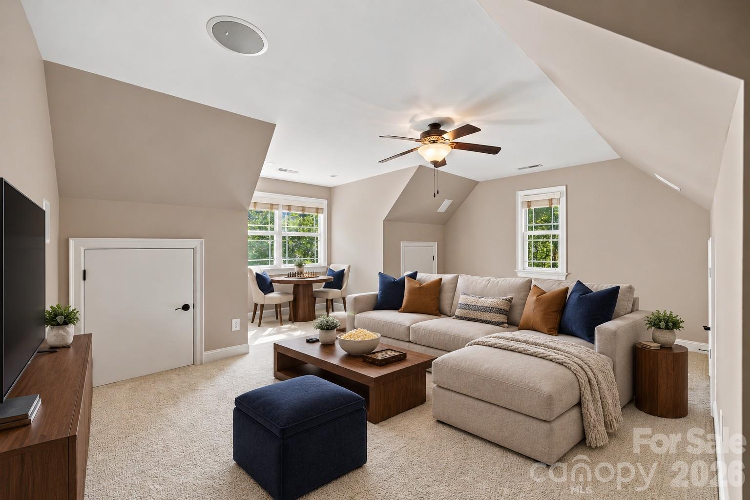 Staged living room with a beige sectional, dark wood coffee table, and dining nook beneath a vaulted ceiling.