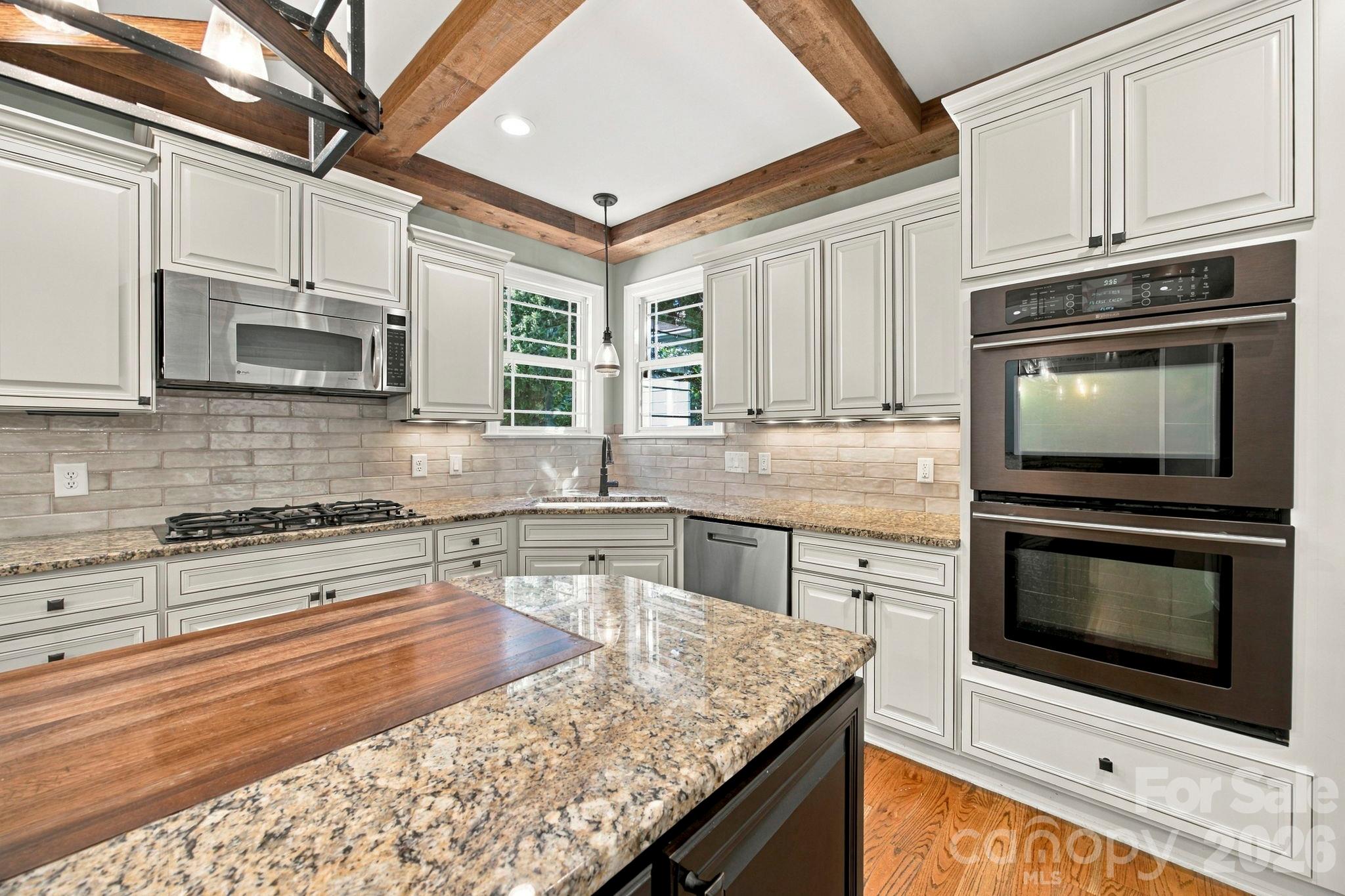 Kitchen with exposed wood beams, white cabinets, granite counters, and a large wood-topped island.