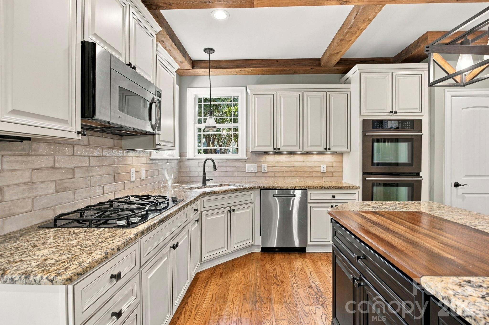 Kitchen with white cabinets, granite counters, stainless steel appliances, exposed wood beams, and a wood-topped island.