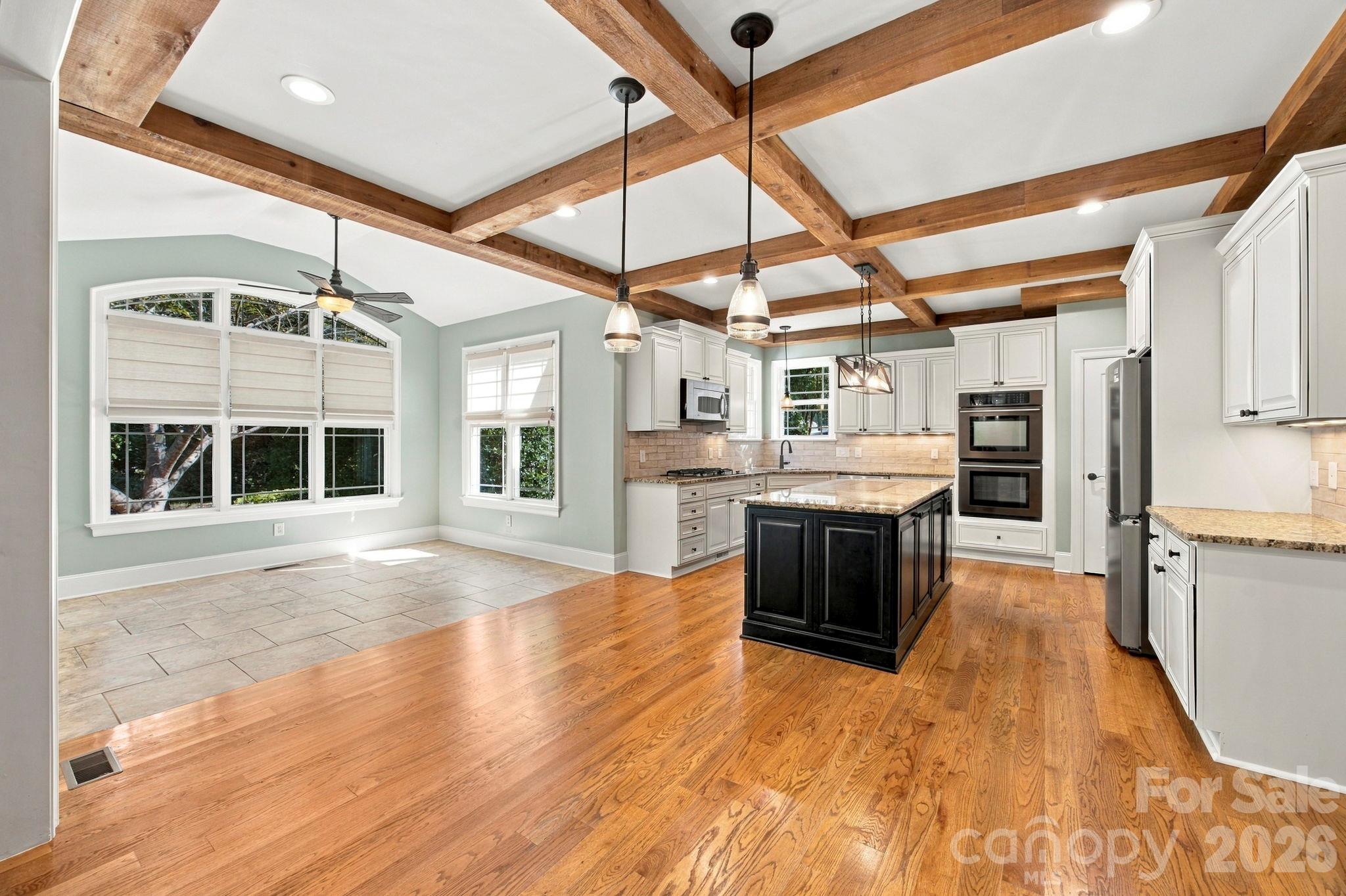 Kitchen with a black island, white cabinets, hardwood floors, and exposed wood ceiling beams.