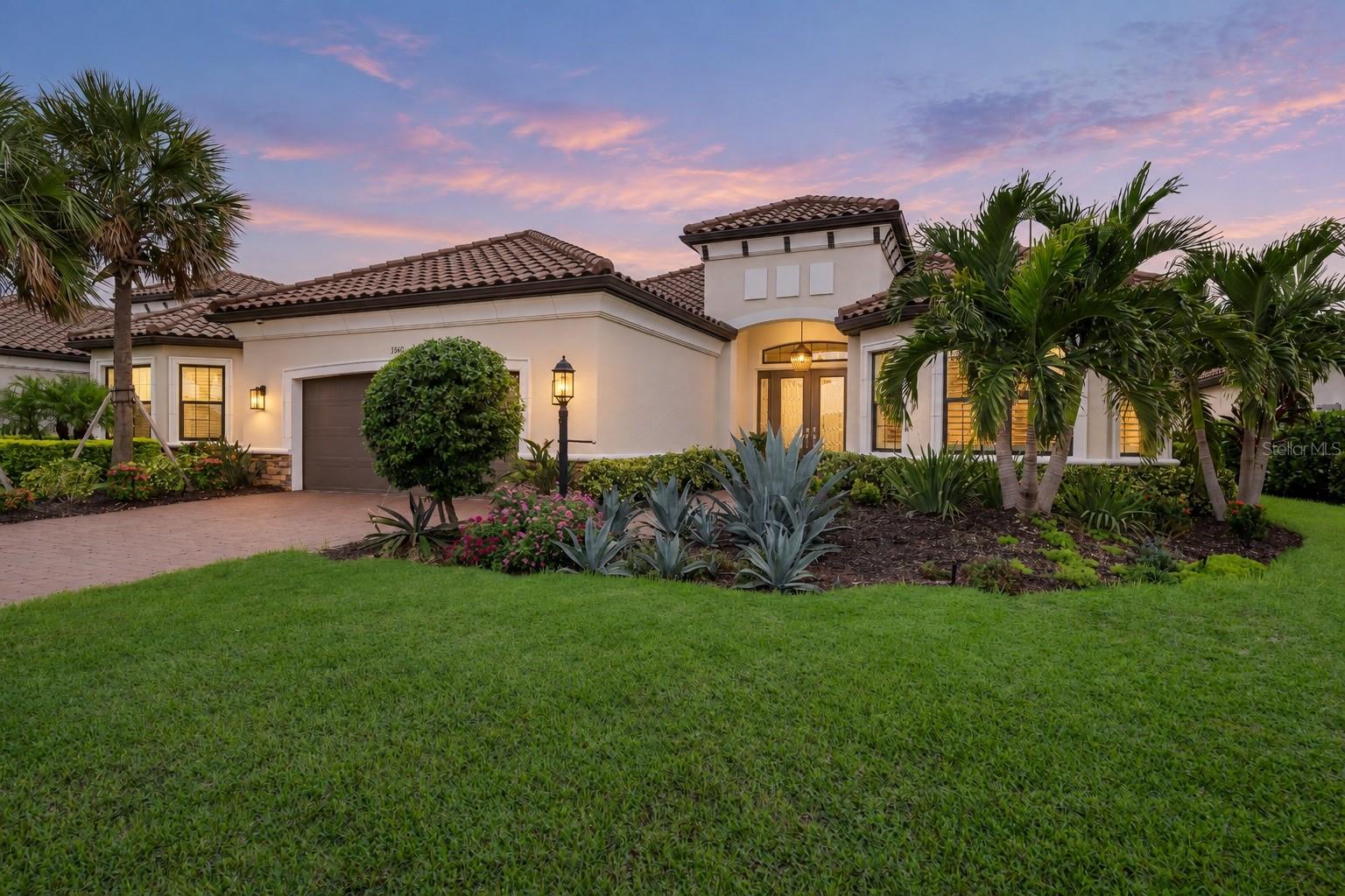 Stucco home with a tiled roof, palm trees, and landscaped gardens at dusk.