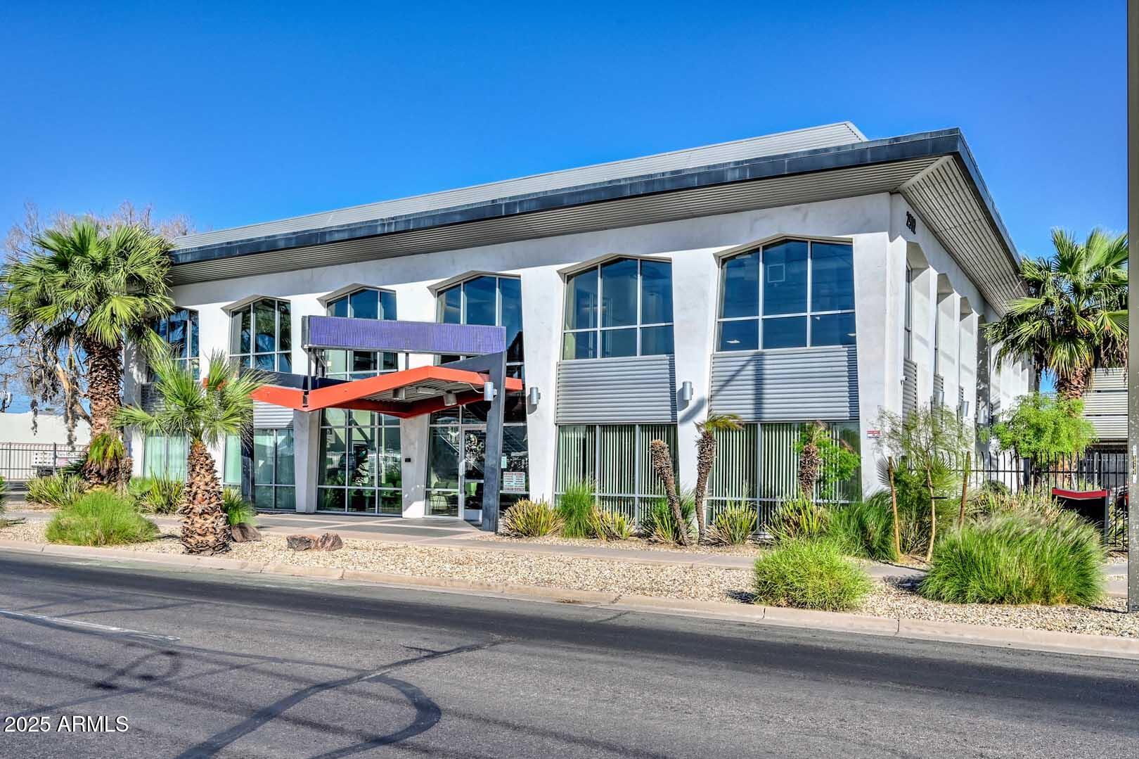 Modern commercial building with tall angular windows, a red entrance canopy, and palm-lined desert landscaping.