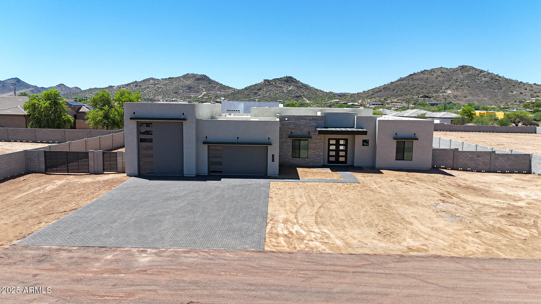 Modern gray home with stone accents and a wide paved driveway, set against desert hills.