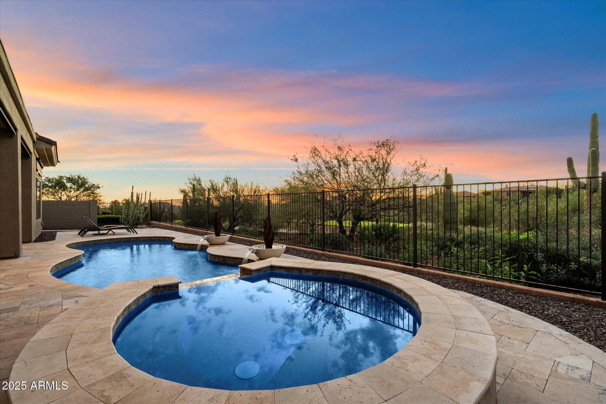 Backyard pool and spa with desert landscaping beneath a pink and blue sunset sky.
