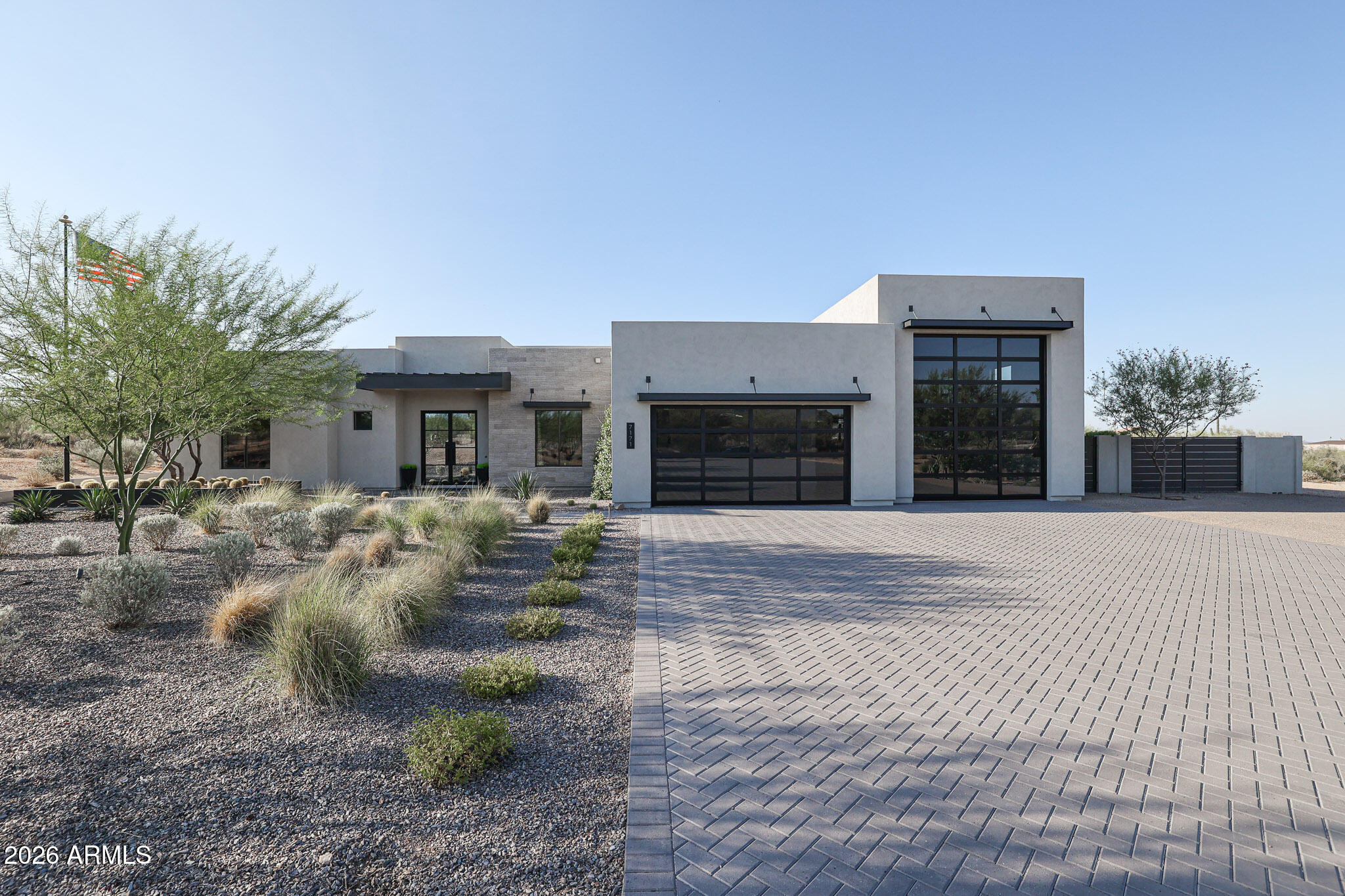 Modern home with tall glass-paneled garage doors, desert landscaping, and a wide paver driveway.
