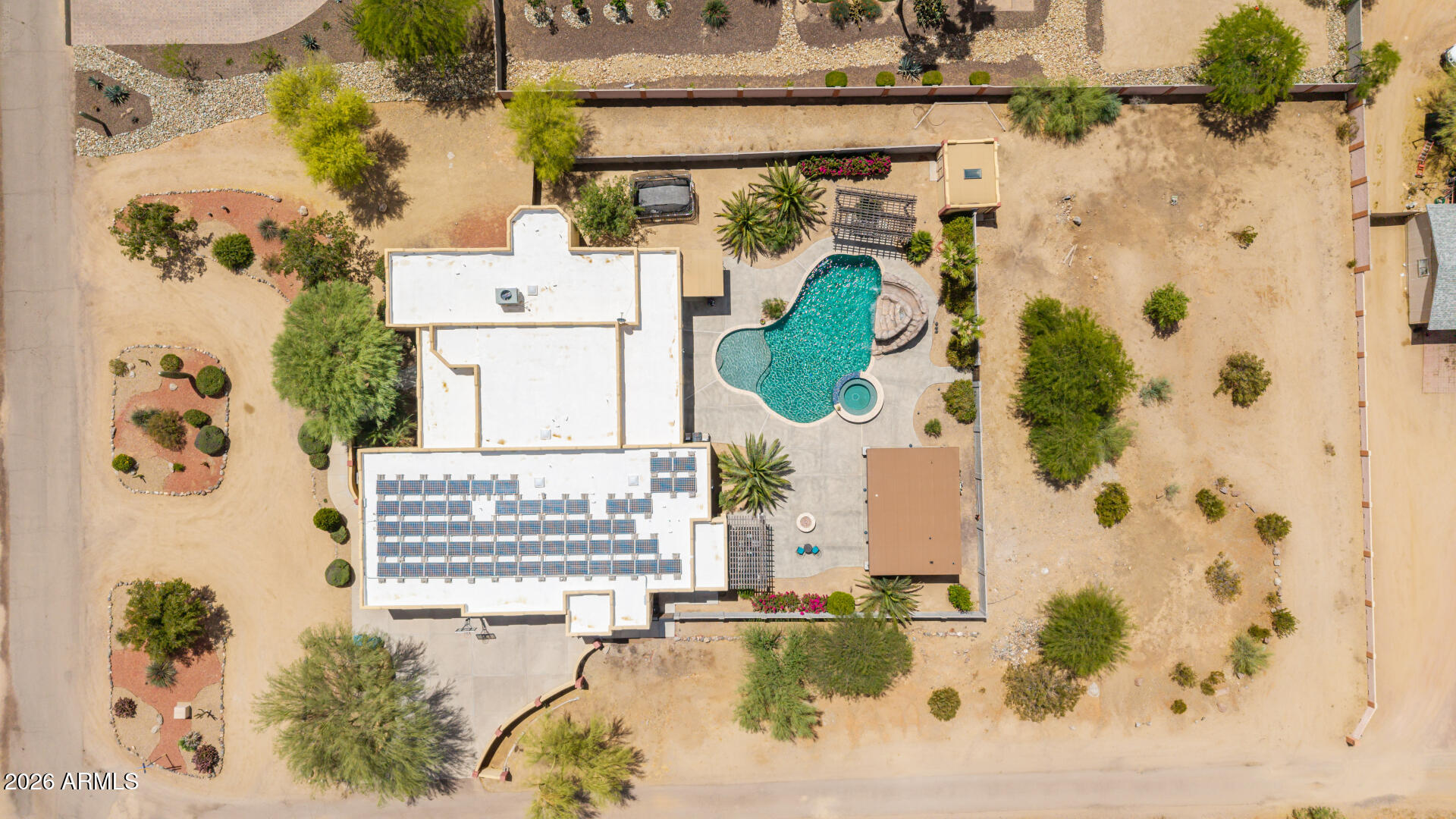 Aerial view of a home with rooftop solar panels, a swimming pool, spa, and expansive desert yard.