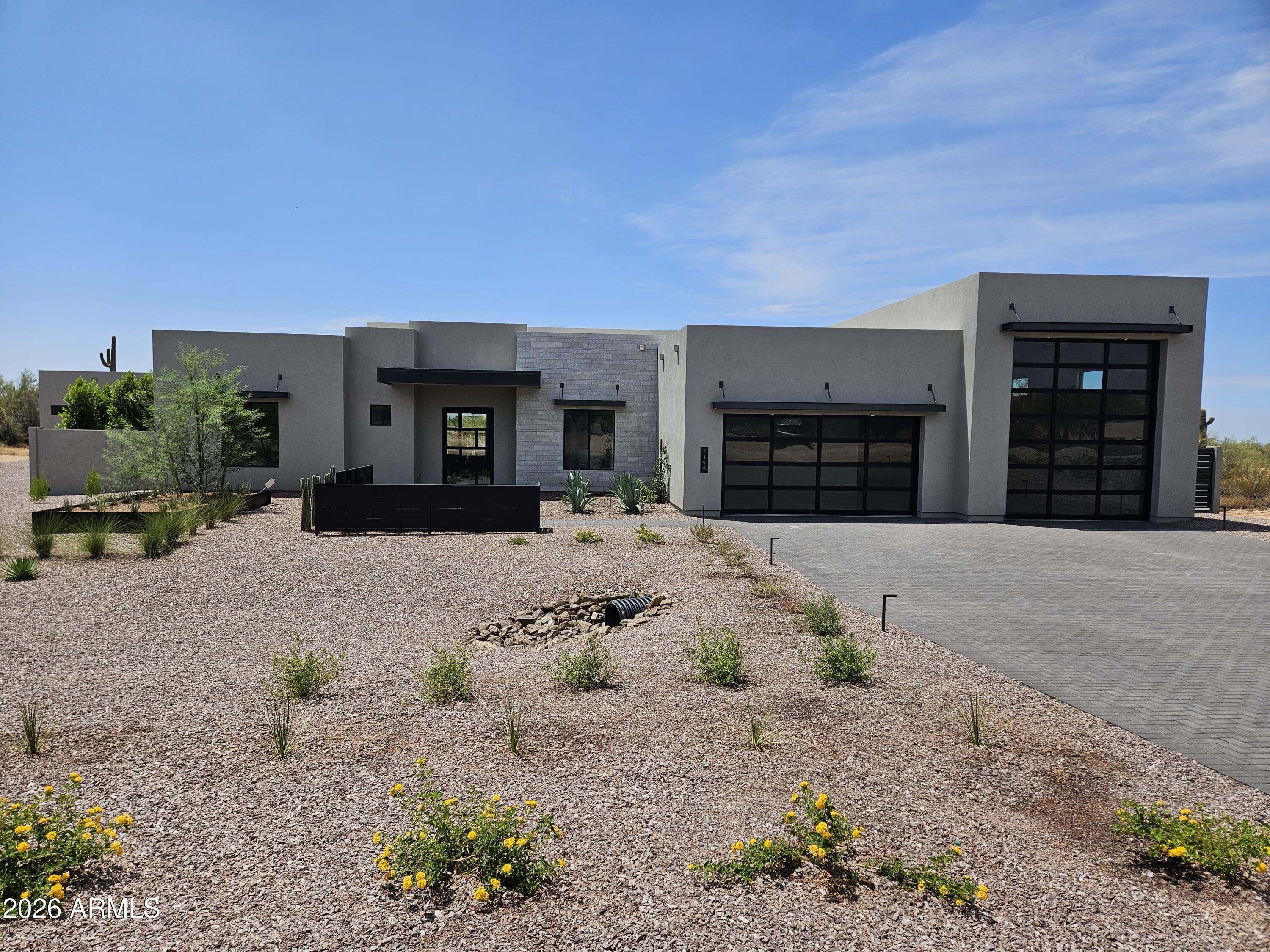 Modern gray desert home with two black glass garage doors and gravel xeriscaping.