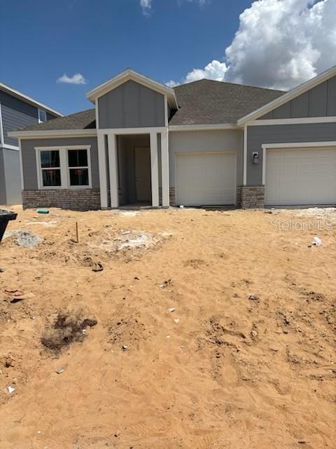 Gray single-story home with a covered entry, attached garage, and bare sandy yard.