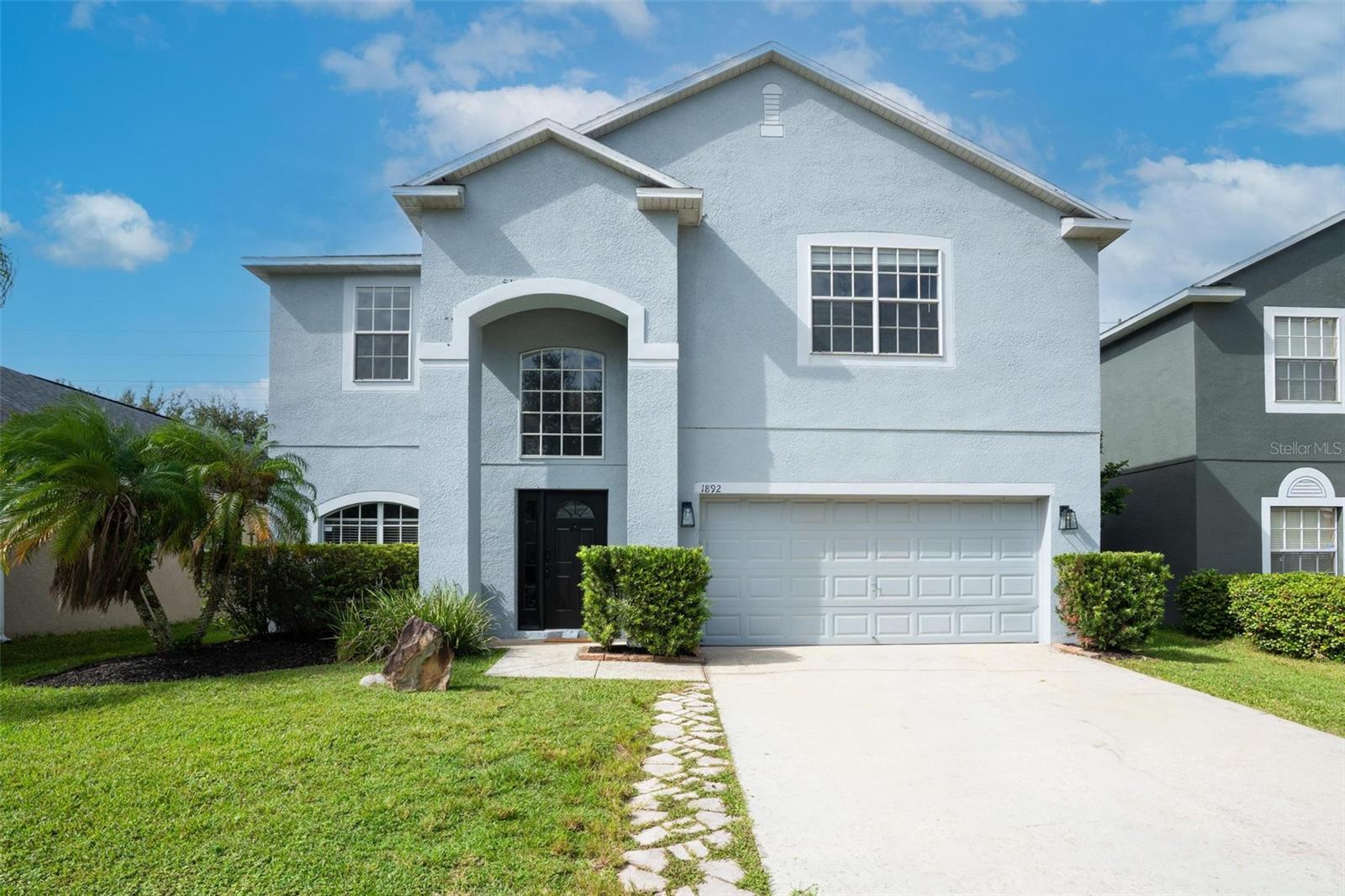 Two-story light-blue house with an arched entry, double garage, and landscaped front lawn.