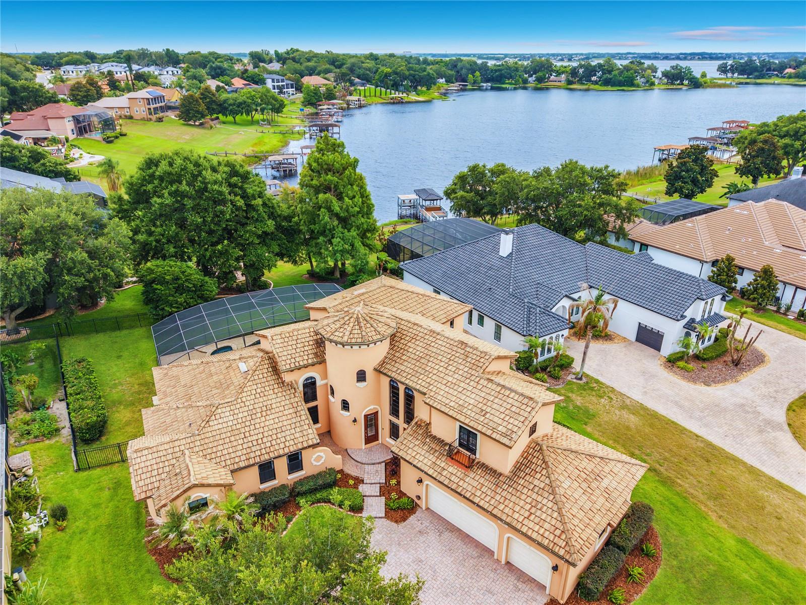 Aerial view of a peach-colored home beside a lake, with tile roofs and a screened pool enclosure.