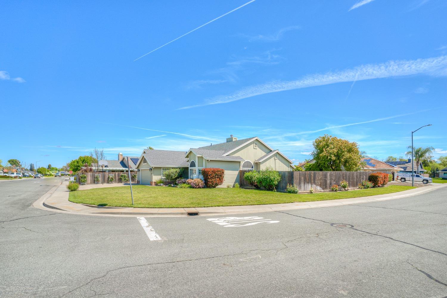 Corner home with pale green siding, landscaped lawn, attached garage, and wooden privacy fence.