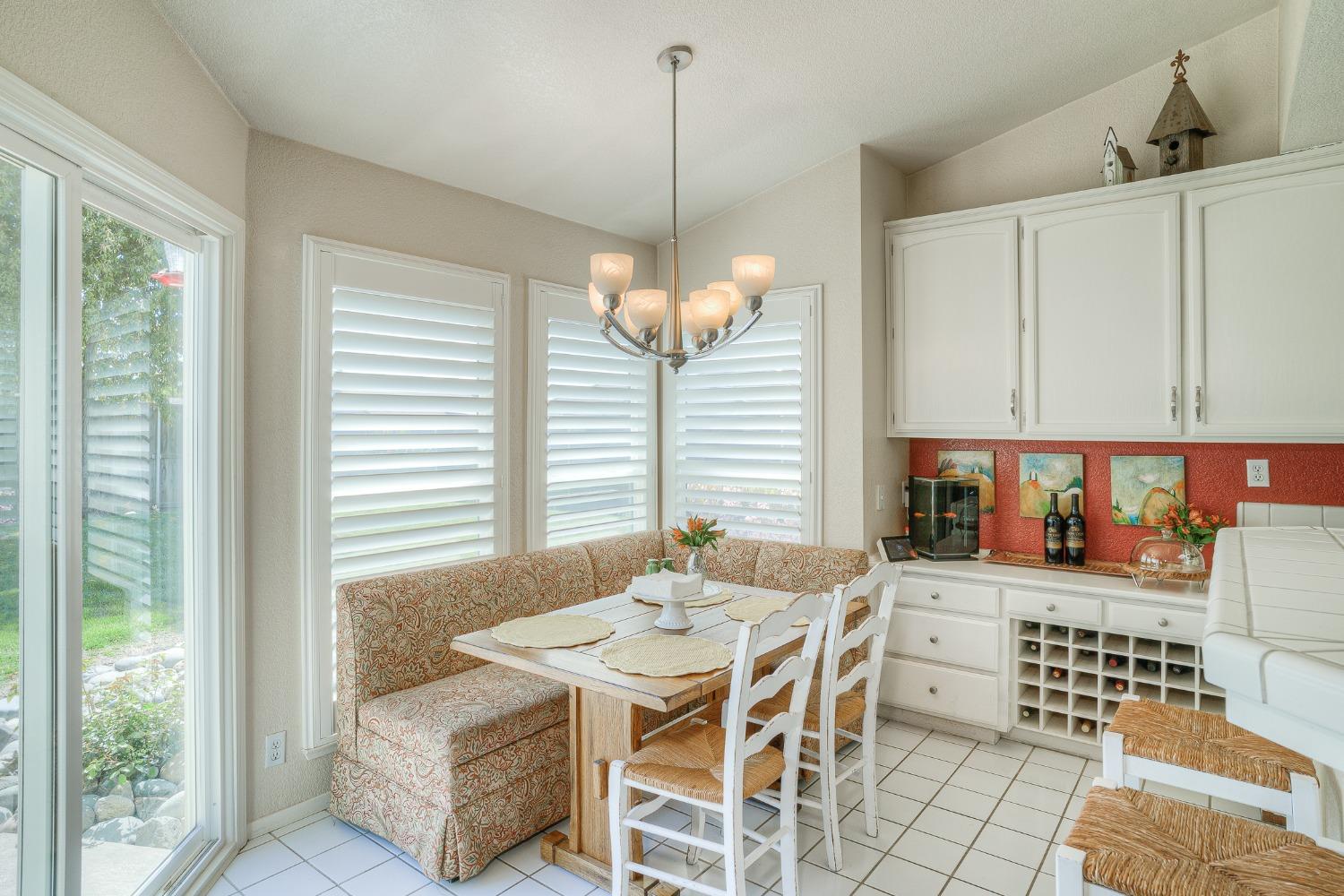 Dining nook with a patterned banquette, white table, plantation shutters, and built-in wine storage.