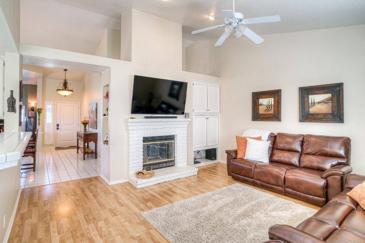 Living room with a white brick fireplace, mounted TV, vaulted ceiling, and brown leather sofas.