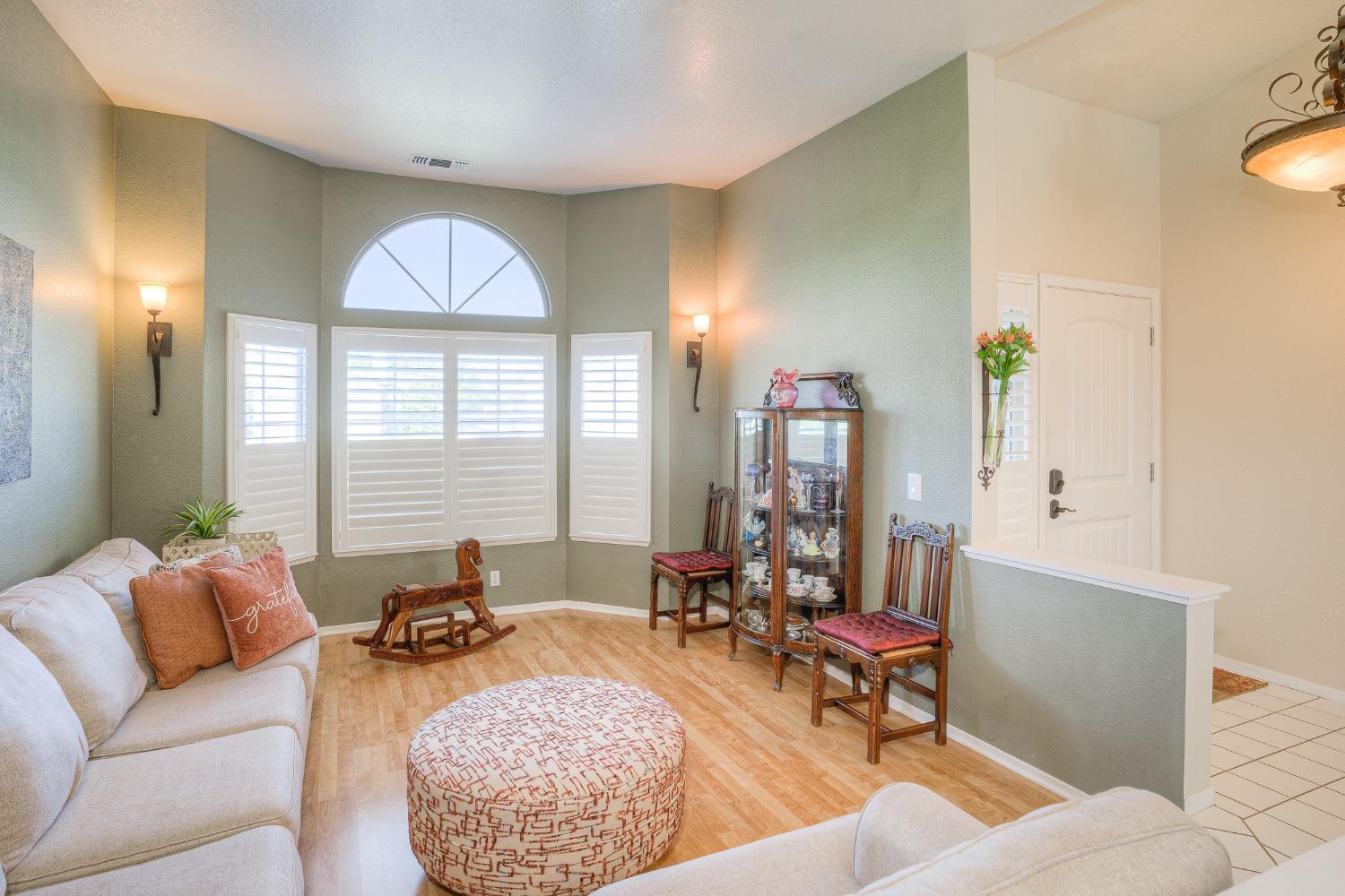 Furnished living room with an arched shuttered window, pale green walls, and light wood flooring.