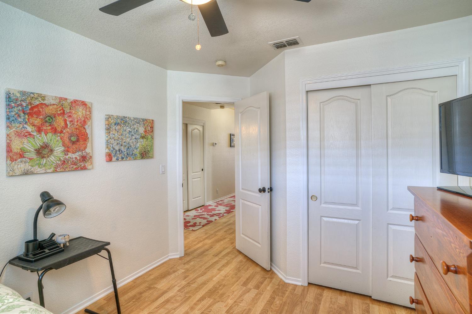 Bedroom with white closet doors, light wood floors, and colorful floral wall art.
