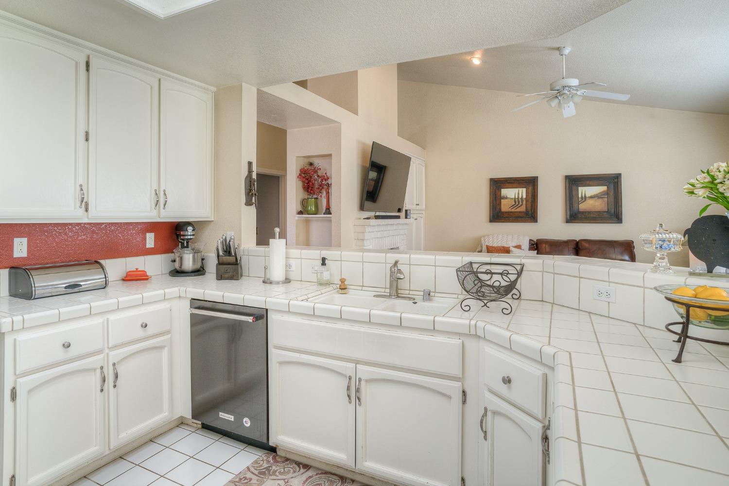 Kitchen with white cabinets, tiled counters, red backsplash, and a view into the living room.