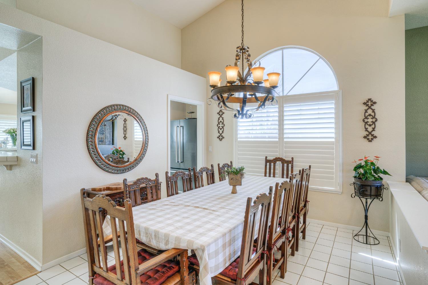 Dining room with a long checked table, carved wooden chairs, and an arched shuttered window.
