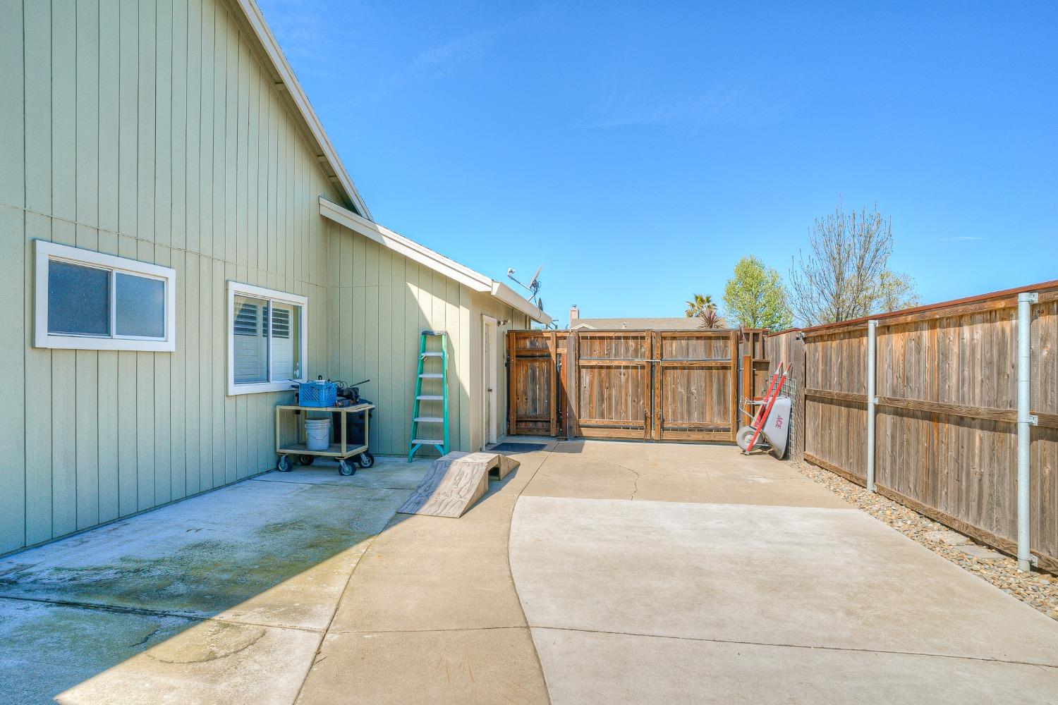 Paved side yard with a concrete patio, wooden fence, and gate beside the house.