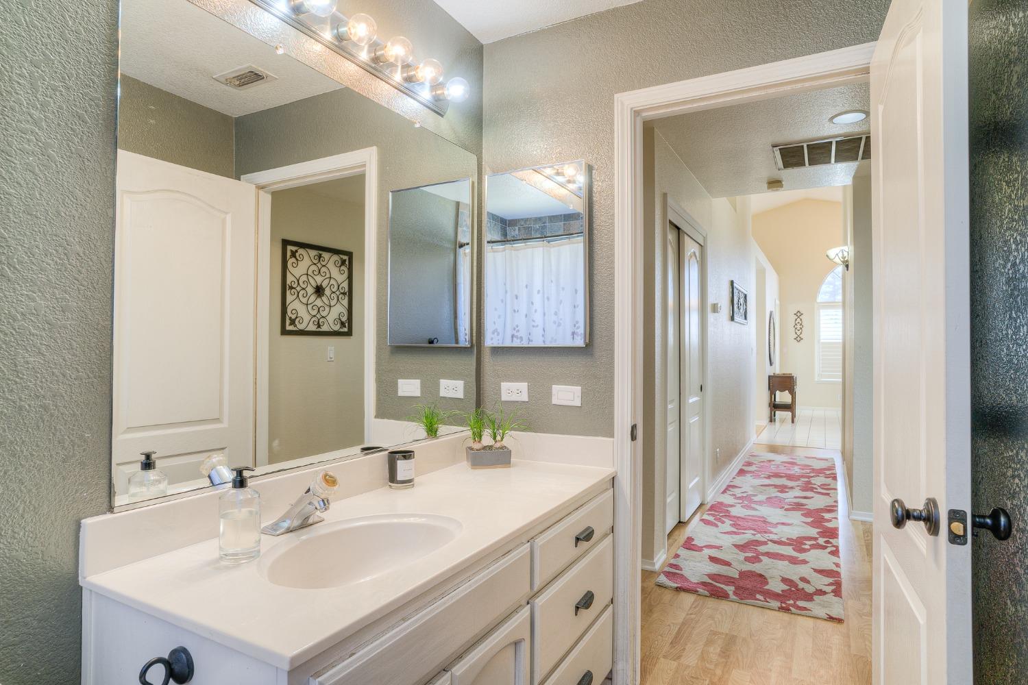 Bathroom vanity with large mirrors and a doorway opening onto a hallway with a patterned runner.