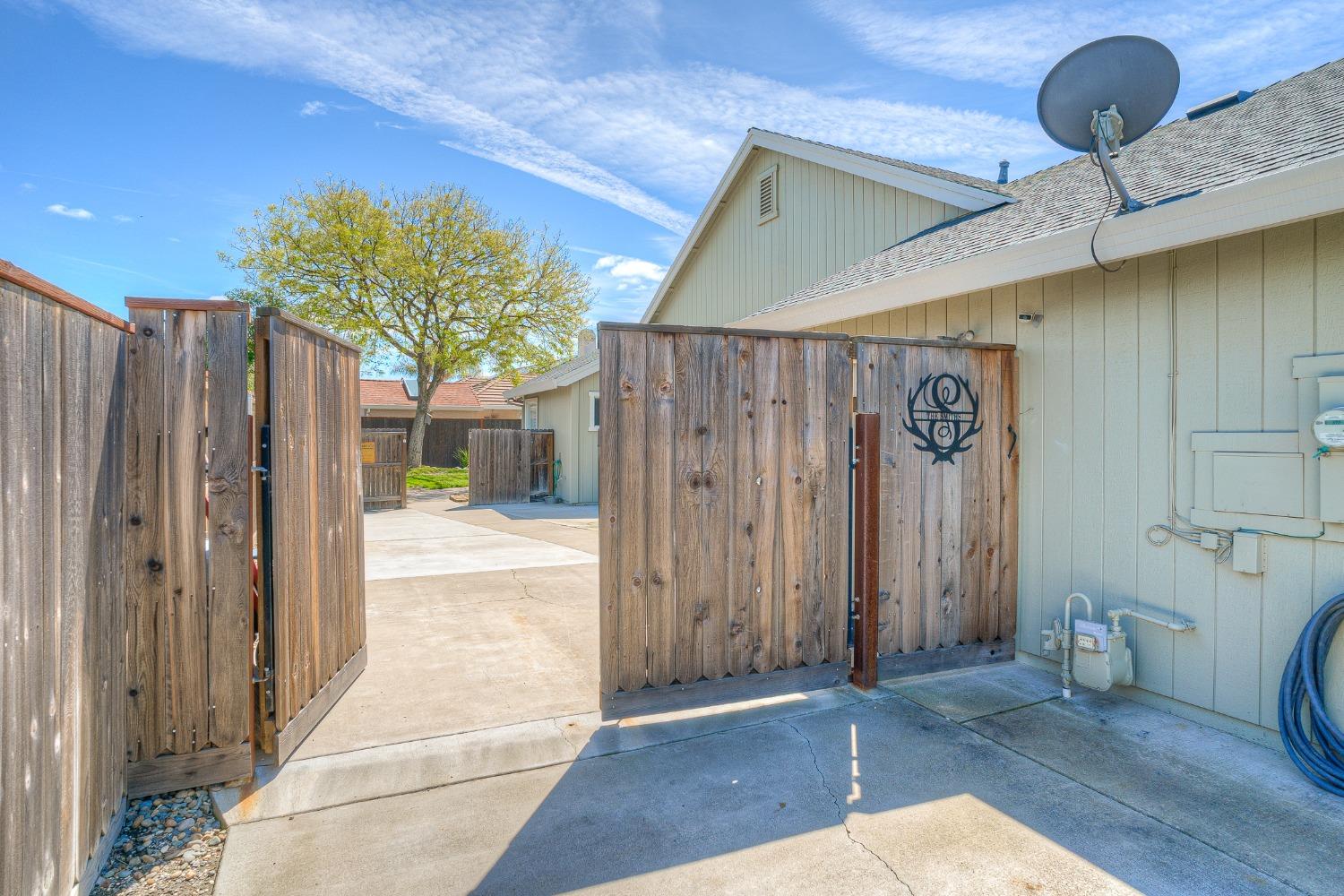 House exterior beside a concrete driveway, with open wooden privacy gates and a satellite dish on the roof.
